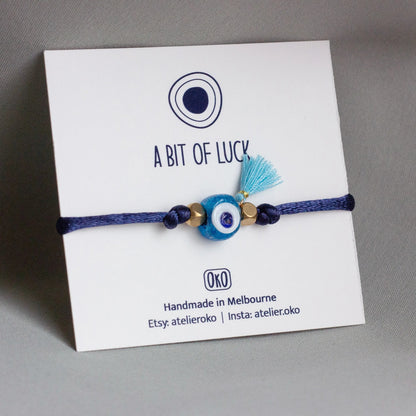 Blue bracelet with evil eye charm on a white card with 'A Bit of Luck'