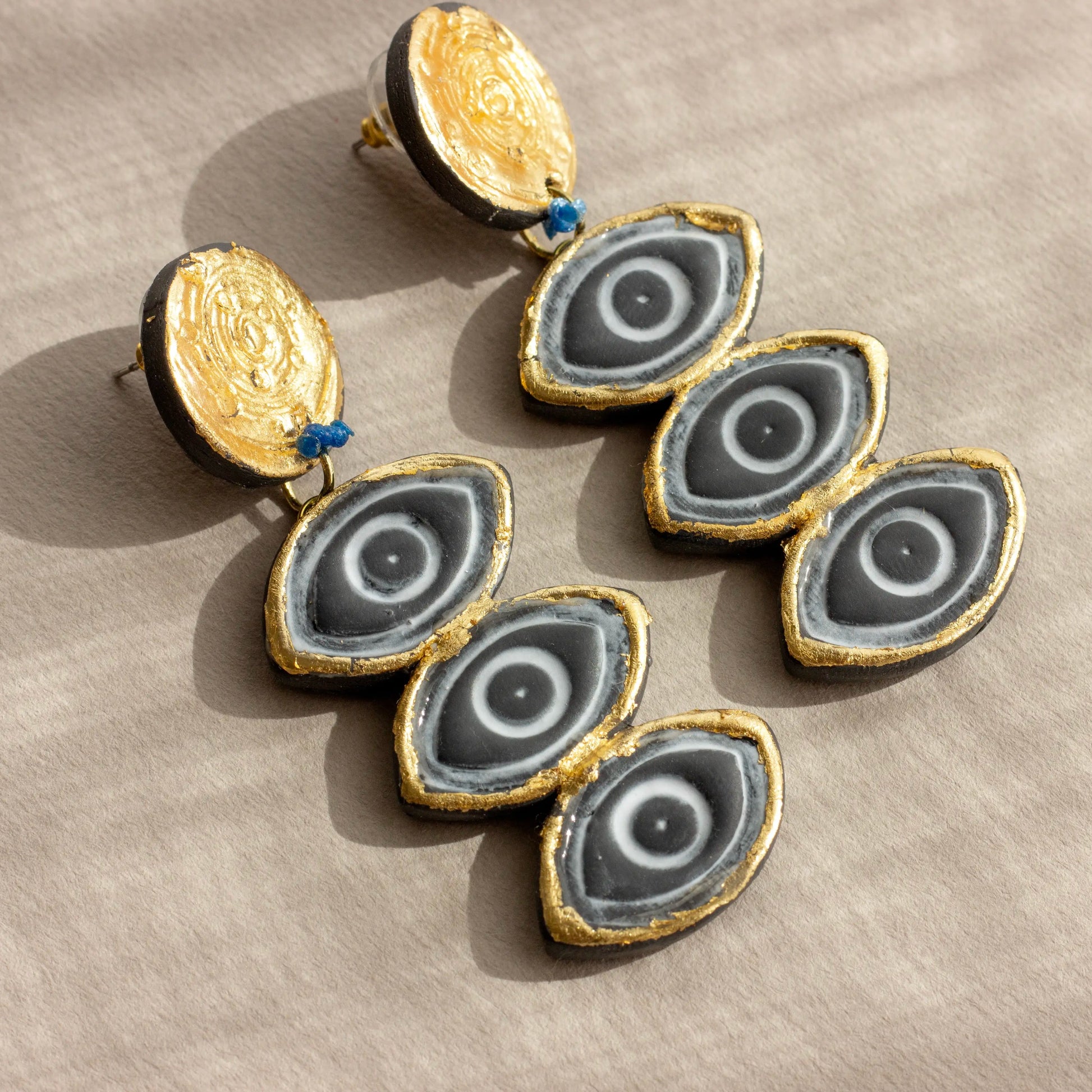 A pair of asymmetric polymer clay earrings with gold and black colors and stainless steel studs.